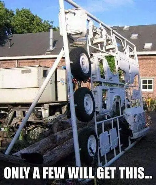 A white utility truck is vertically stacked on top of itself, held upright by a metal frame, with its wheels and body parts…