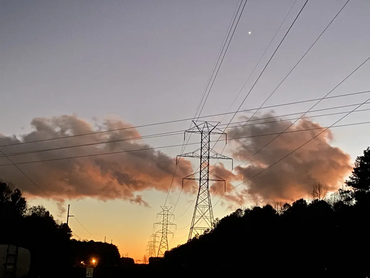 A photo of power line towers silhouetted against a sunset sky with orange clouds and a visible moon. The overlaid text reads…
