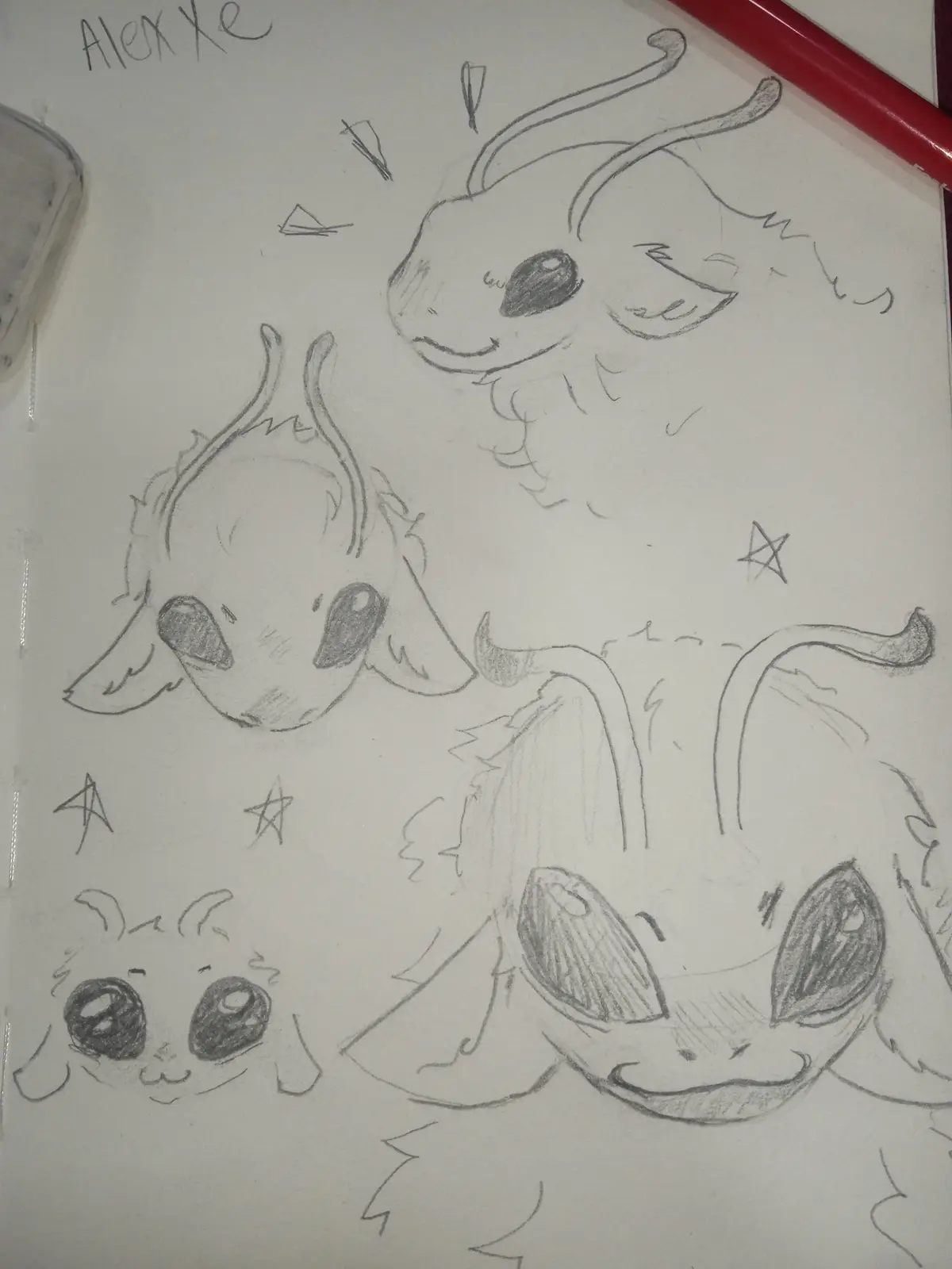 A pencil sketch on paper shows four different cute, fluffy, cartoon-style creature heads with large eyes and horns or…