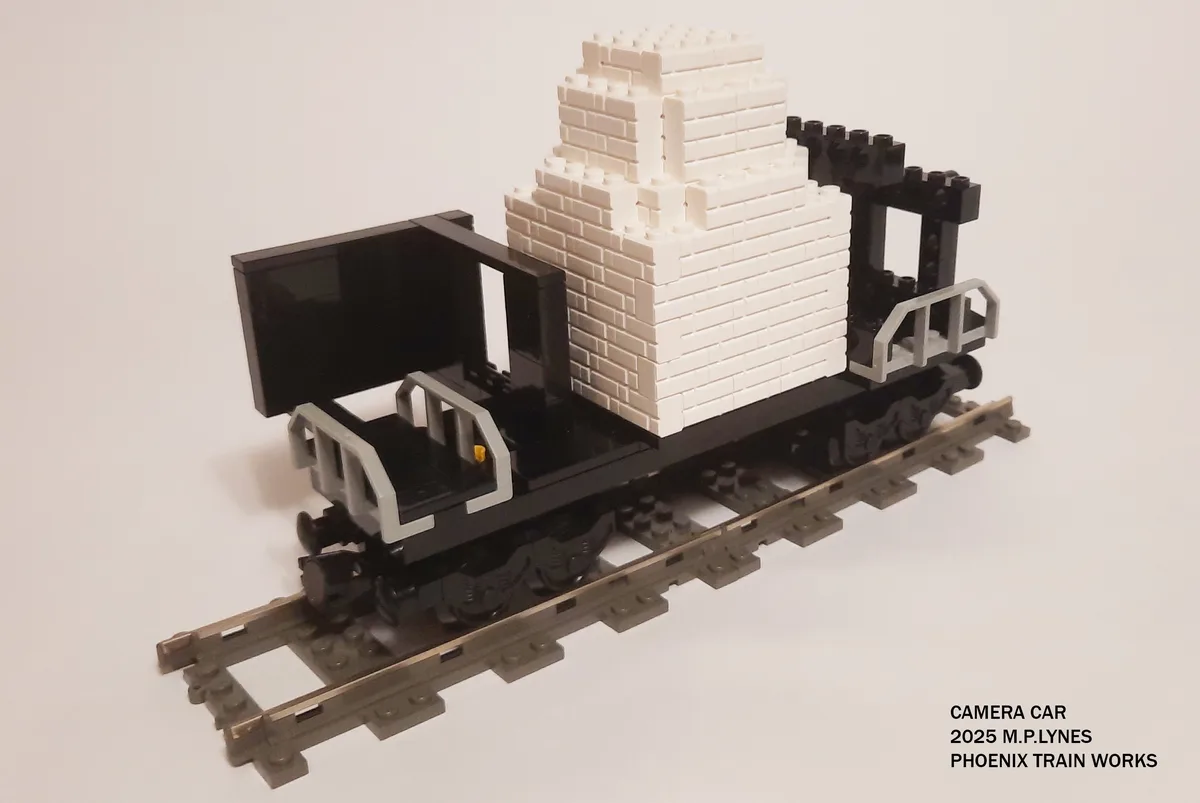 A Lego model of a train car on tracks, carrying a large white Lego structure resembling a pyramid or stepped monument. The…