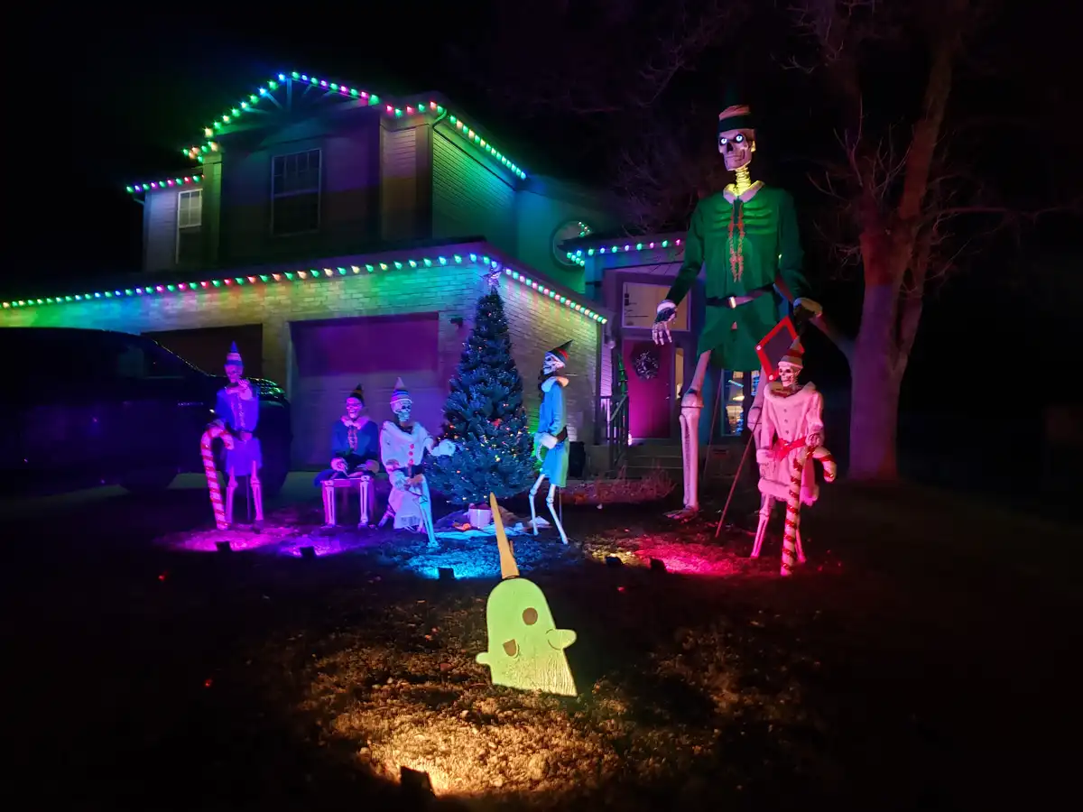 A nighttime photo of a house decorated with colorful lights, featuring several skeleton figures dressed as elves gathered…