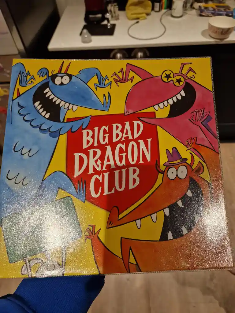A colorful children's book cover titled 'BIG BAD DRAGON CLUB' features three cartoon dragons: a blue one with horns and…