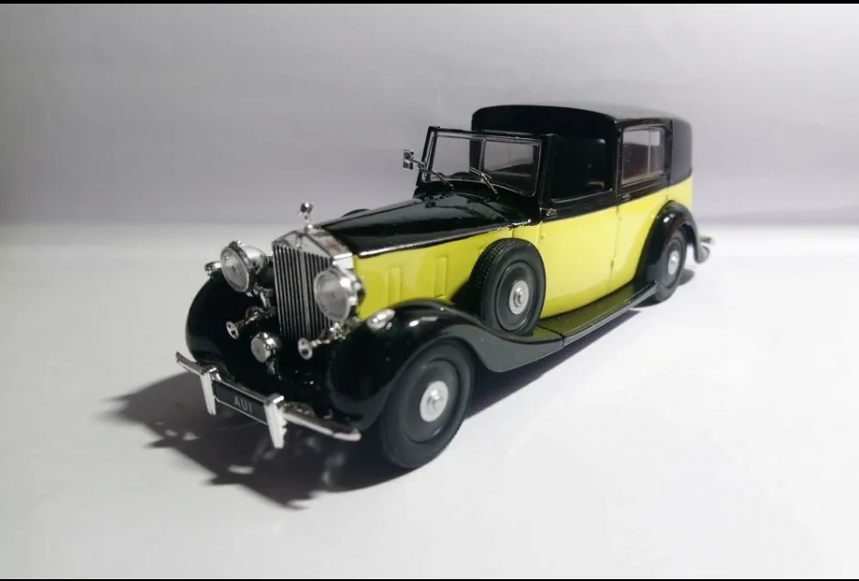 A vintage-style die-cast model car with a black roof and bright yellow body, shown from a three-quarter front angle against…