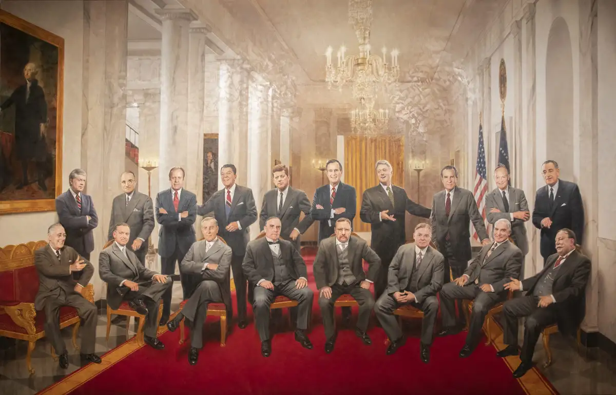 A formal group portrait of multiple U.S. presidents in a grand hall with marble columns and a chandelier, seated and…