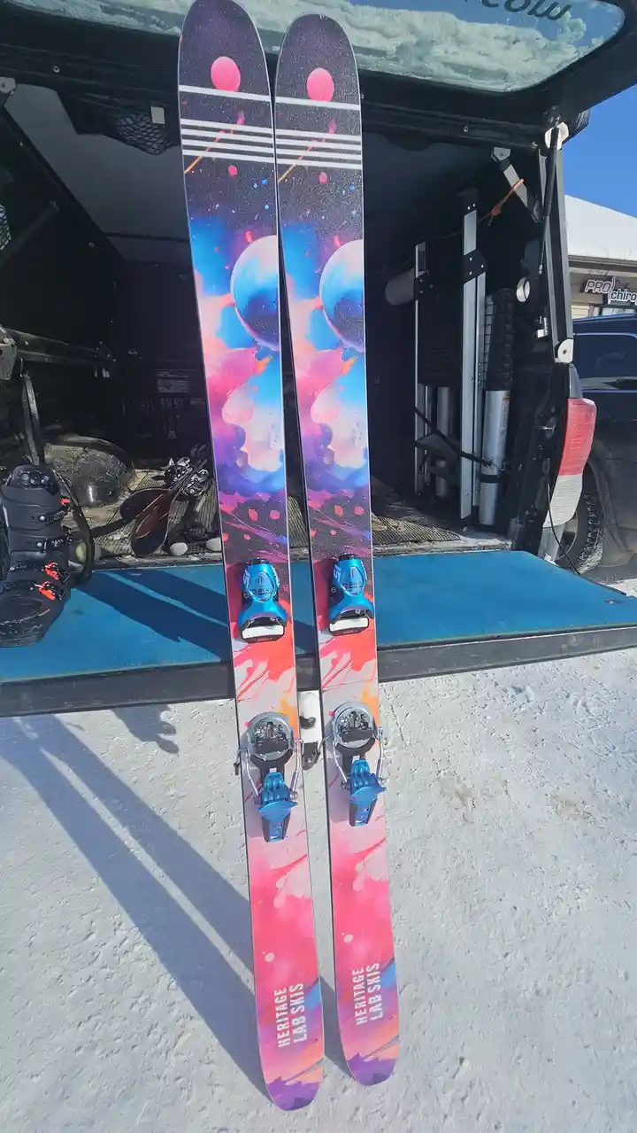 A pair of brightly colored skis with a cosmic galaxy design featuring pink, blue, and purple nebulae and planets are…