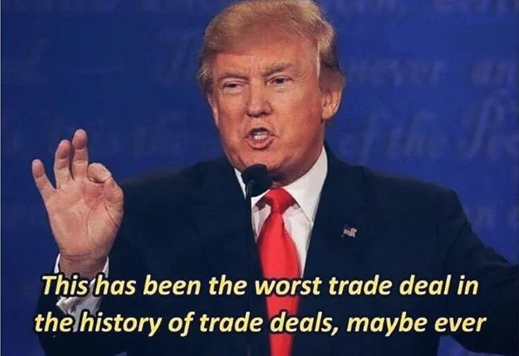 A photo of Donald Trump speaking at a podium with a blue background, gesturing with his right hand. He wears a dark suit…