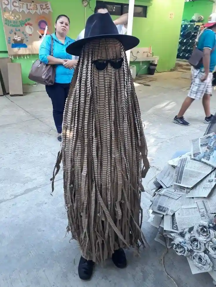 A person is dressed in a costume made of brown, corrugated cardboard strips, resembling a ghost with long, dangling strands…