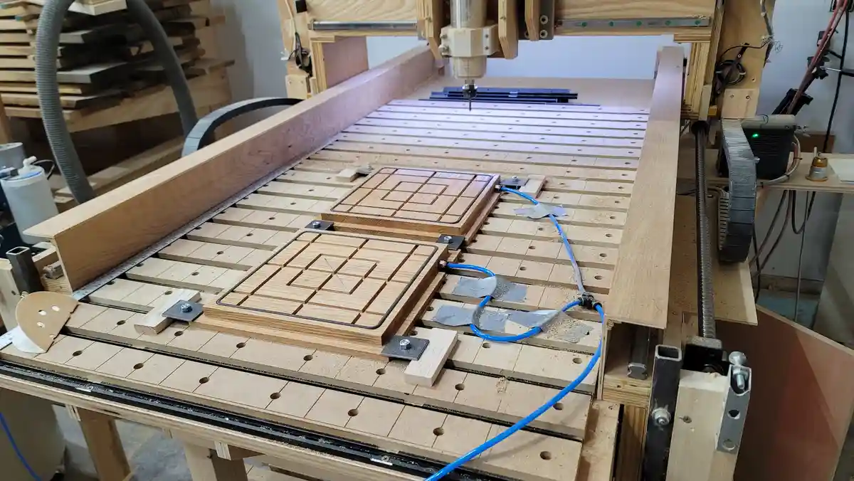 A woodworking CNC machine is actively carving a wooden chessboard that also features a tic-tac-toe grid, with blue tubing…
