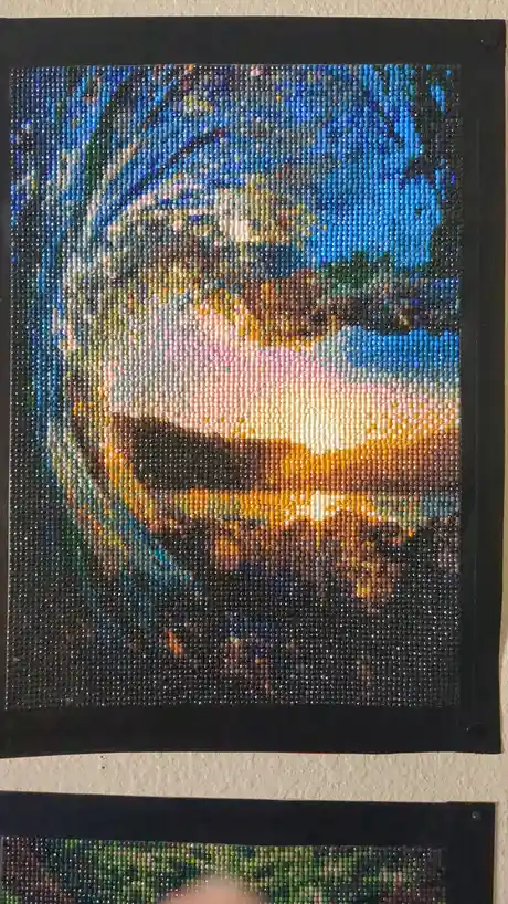 A completed bead mosaic artwork depicting a person with a bright, colorful face and dark hair, mounted in a black frame on a…