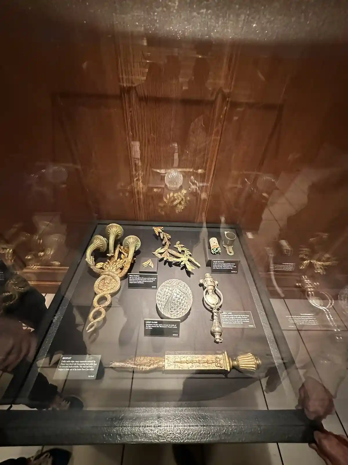 A museum display case with various ornate, golden ship fittings and artifacts, including a bedpost, light globe, and…