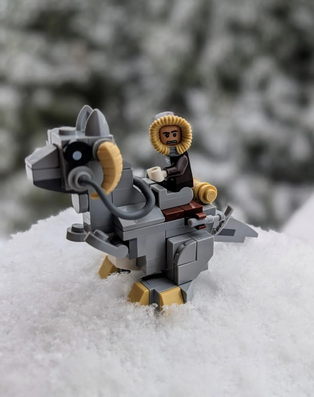 A lego minifigure wearing a fur-lined hood and holding a mug sits atop a gray lego creature with curved horns, standing in…