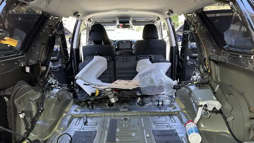 The image shows the interior of a car stripped down to its bare metal frame, with doors and panels removed, exposing wiring…