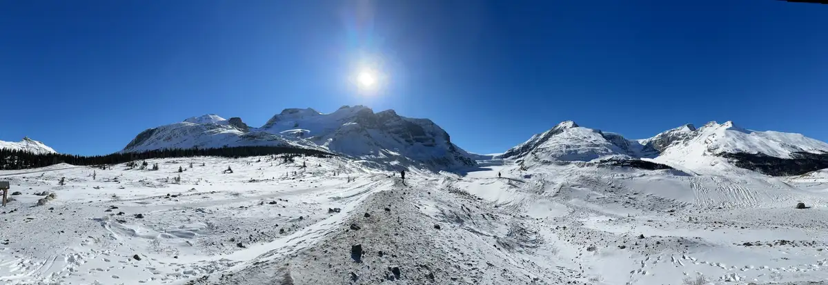 A wide, snowy mountain panorama under a bright sun with two tiny hikers on a trail. The overlaid text reads 'i'm not lazy…