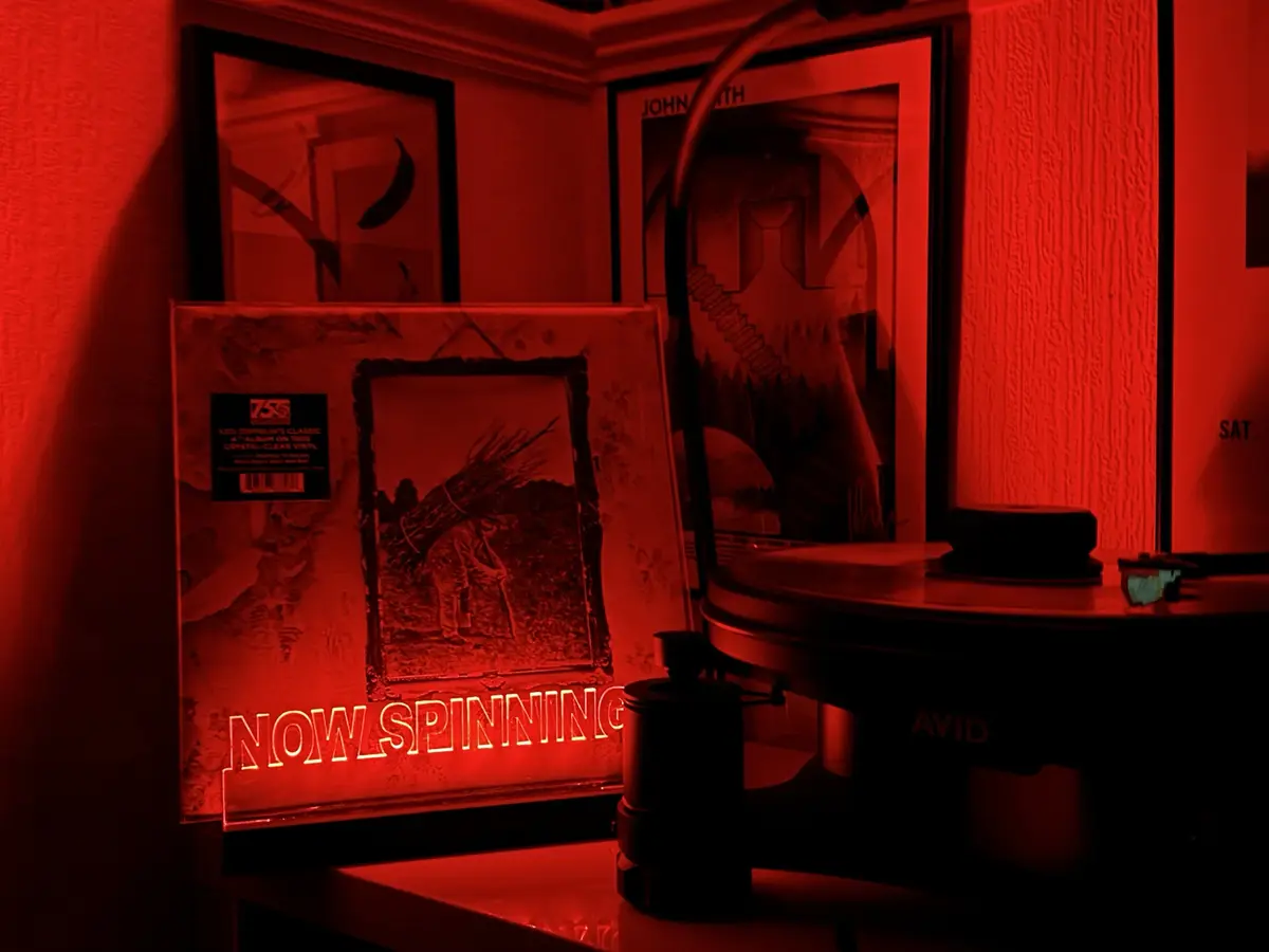 A dimly lit room bathed in red light features a vinyl record player with a record on it, next to a framed Led Zeppelin album…