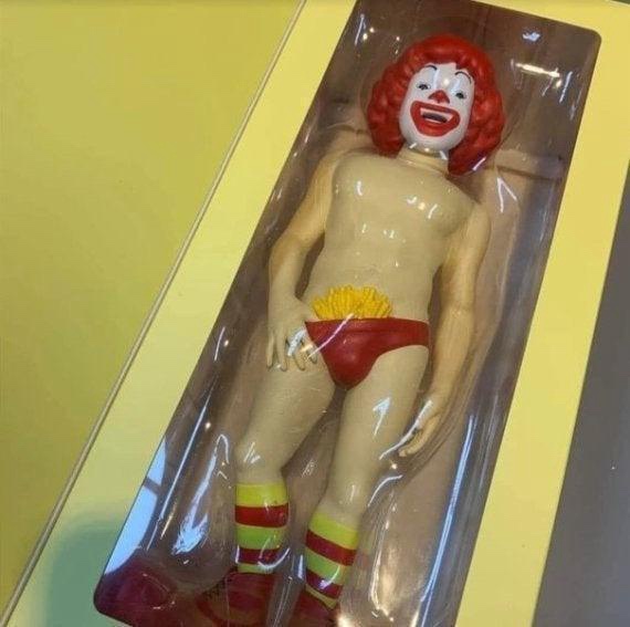A plastic Ronald McDonald action figure is shown in its original packaging, but it's unclothed except for red underwear…