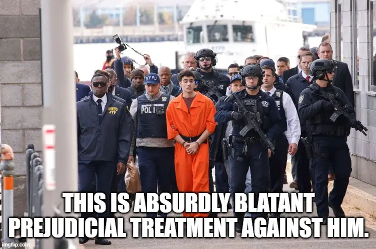 A young man in an orange prison jumpsuit is being escorted by multiple armed police officers in tactical gear. The officers…