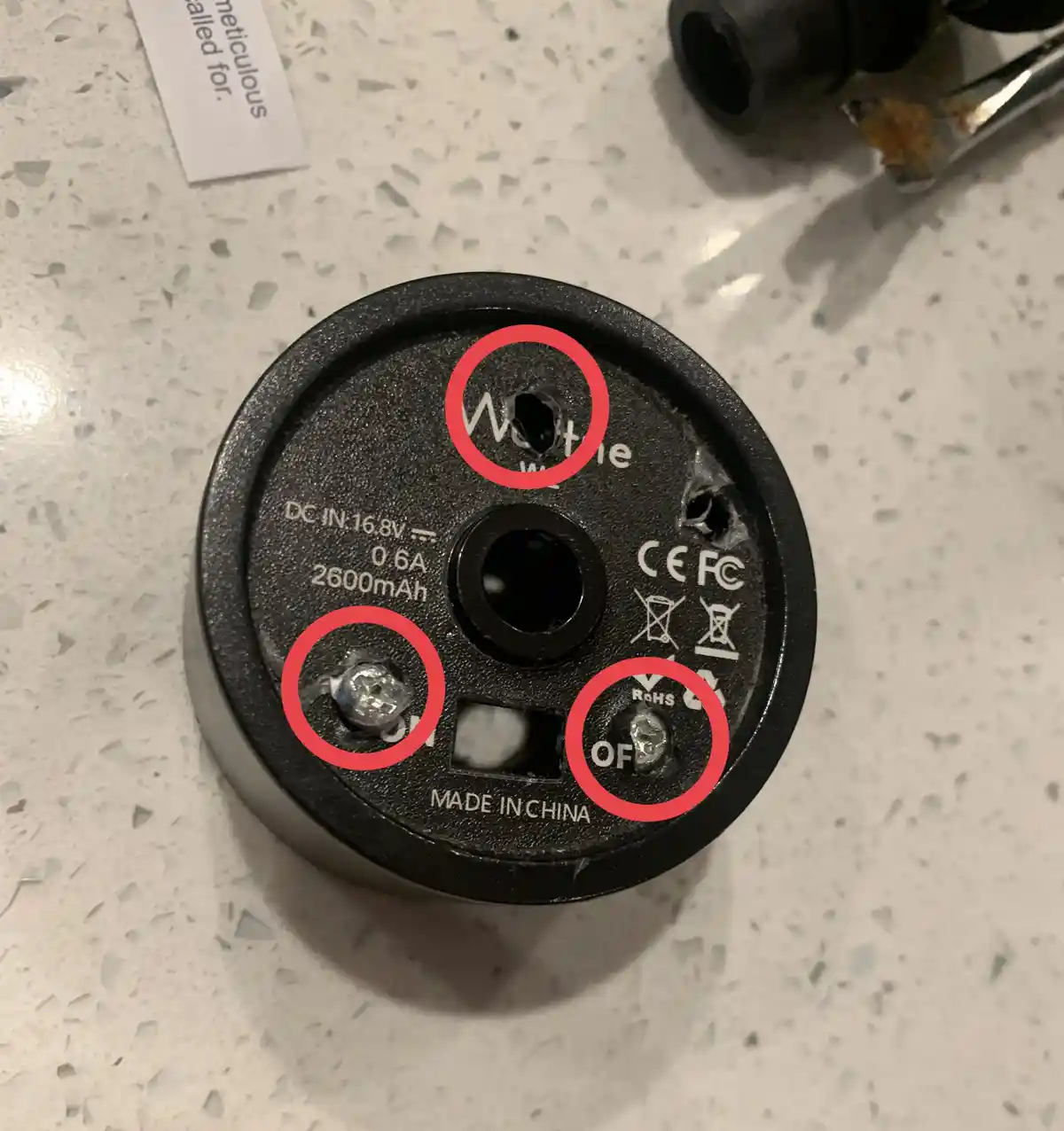 A close-up of a black, circular electronic device, likely a power bank or battery, with three areas circled in red: a hole…