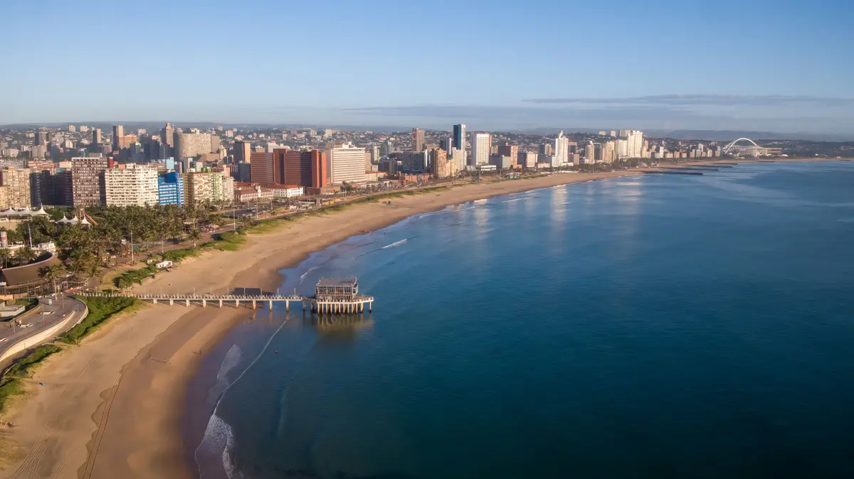An aerial photo shows a wide sandy beach next to a city skyline with many buildings, a pier extending into the ocean, and…