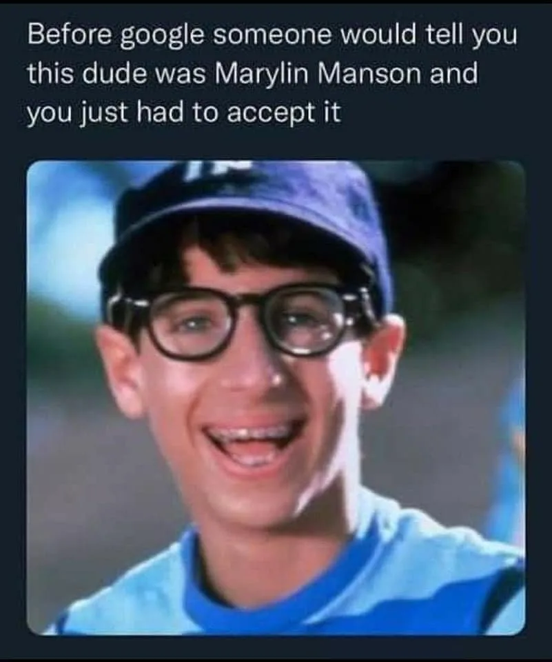 A close-up photo of a young man with dark-rimmed glasses, braces, and a blue baseball cap, smiling broadly while wearing a…
