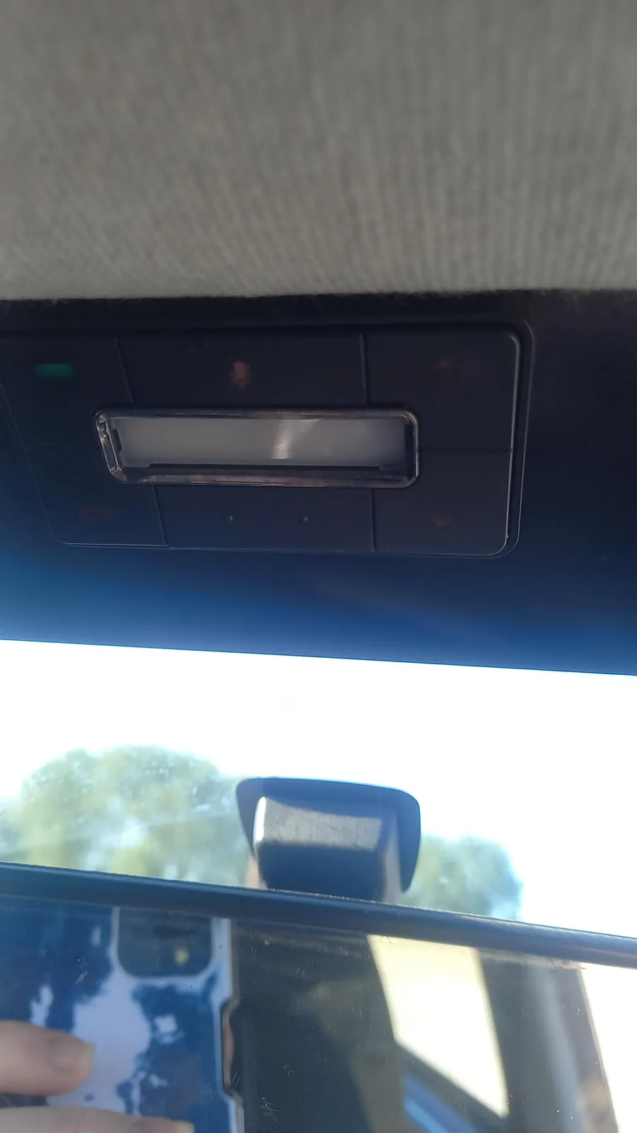 A close-up photo from inside a car shows a person holding a smartphone with a blue and white case, partially visible through…