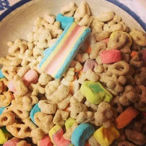 A close-up photo of a bowl filled with cereal pieces and colorful rainbow marshmallows, with one large rainbow marshmallow…