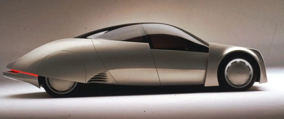 a sleek, silver, futuristic concept car with a curved, aerodynamic body, red taillight, and minimalist design is shown in…