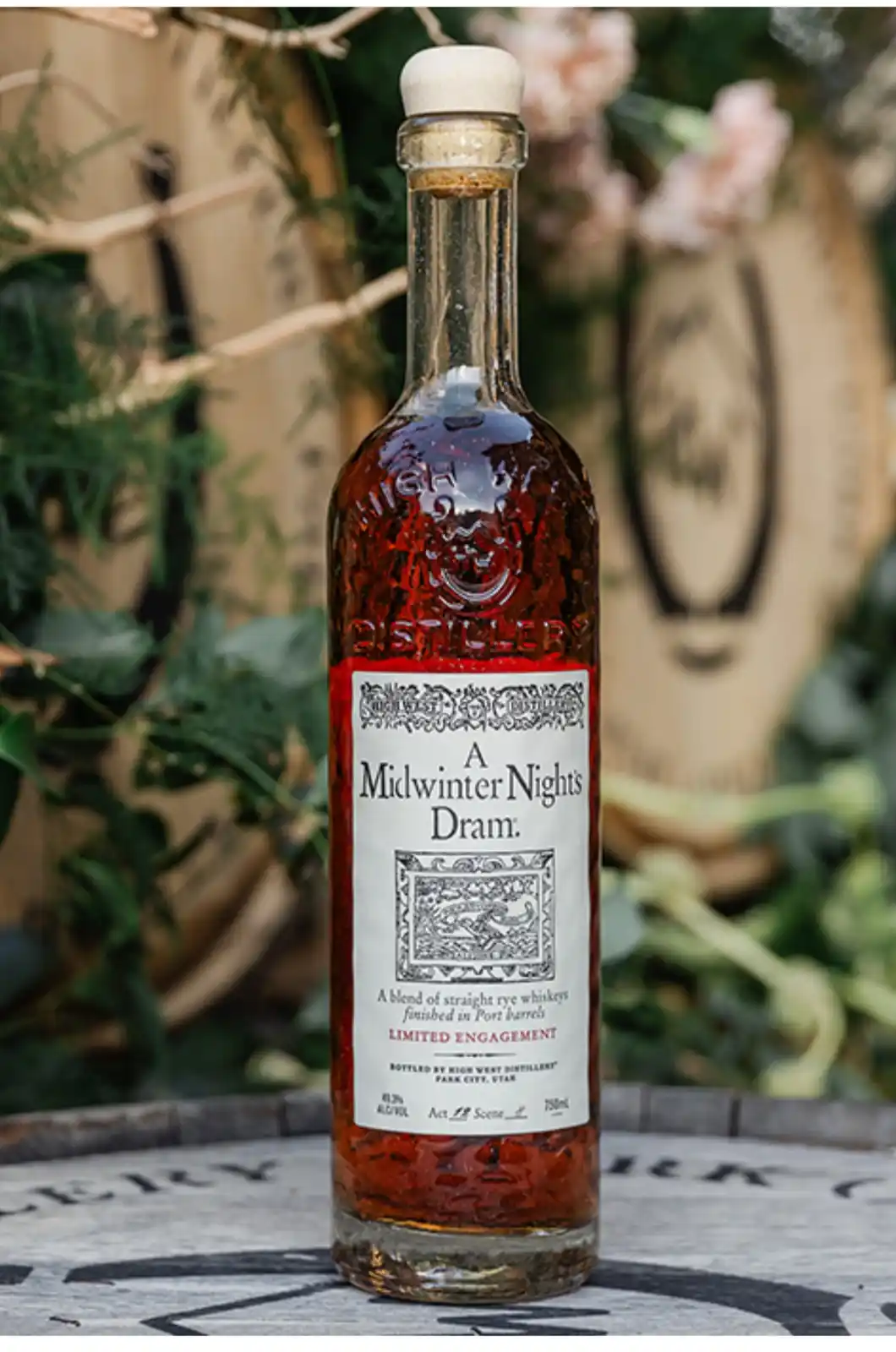 A bottle of whiskey labeled 'A Midwinter Nights Dram' sits on a barrel, with the text 'LIMITED ENGAGEMENT' visible on the…