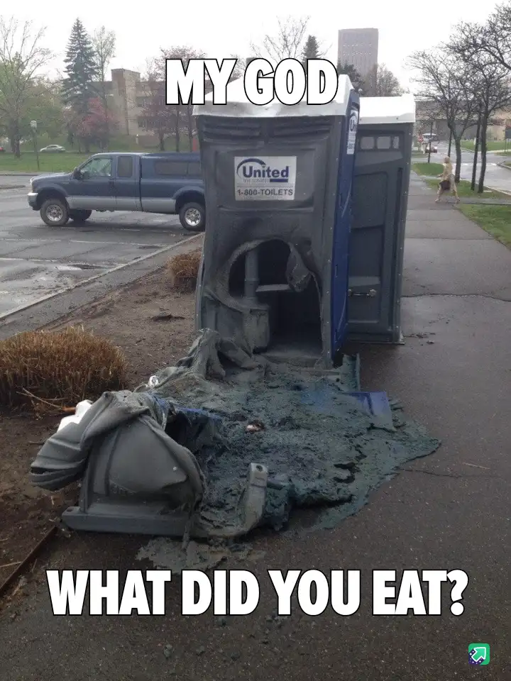 A destroyed portable toilet lies on its side on a sidewalk, its interior and exterior ripped apart with debris and a dark…