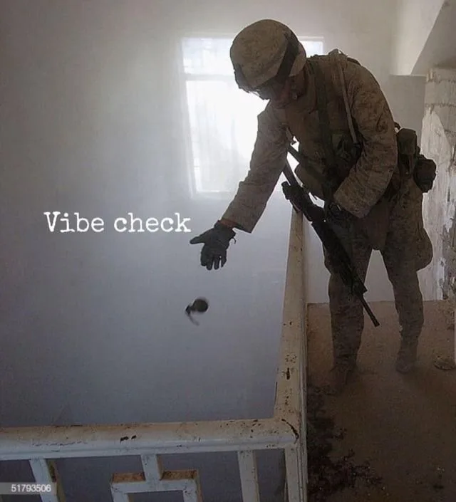 A soldier in full combat gear, holding a rifle, leans over a railing and extends a gloved hand toward a small dark object…
