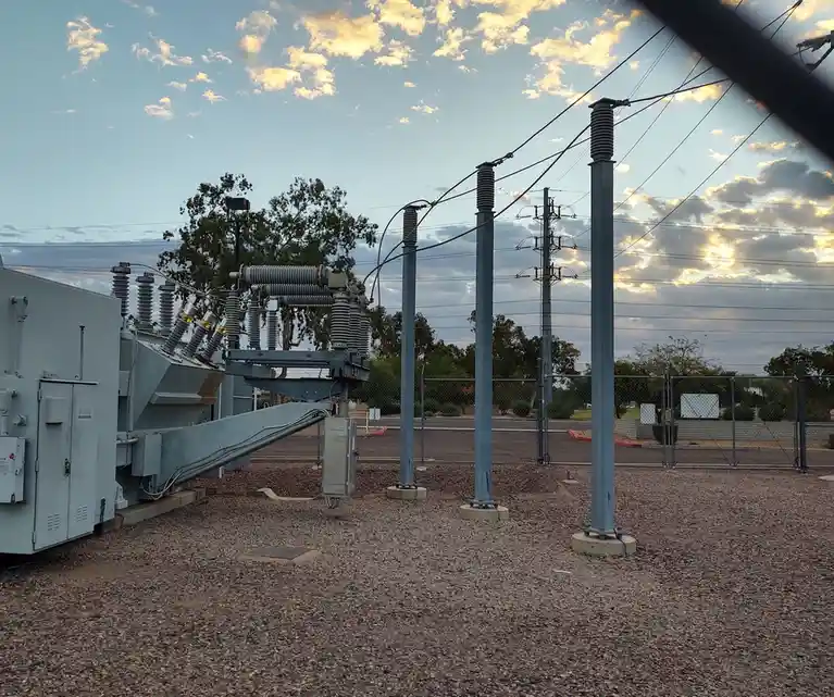 An outdoor electrical substation with large gray transformers, insulators, and metal poles under a partly cloudy sky at…