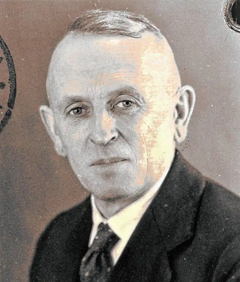 A vintage, grainy black-and-white portrait of a balding, serious-looking man in a suit and tie, with overlaid text reading…