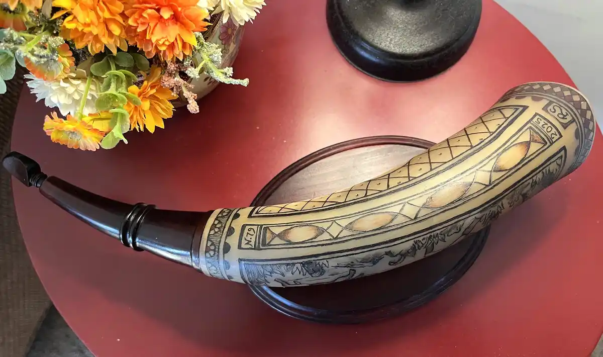 A decorated horn, likely a ceremonial or decorative piece, rests on a dark wooden dish atop a red table. It features…