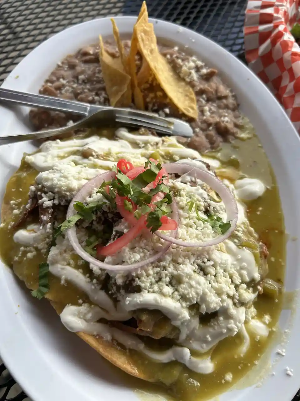 A close-up photo of a plate of Mexican food, featuring a large, round tortilla covered in green sauce, crumbled white…