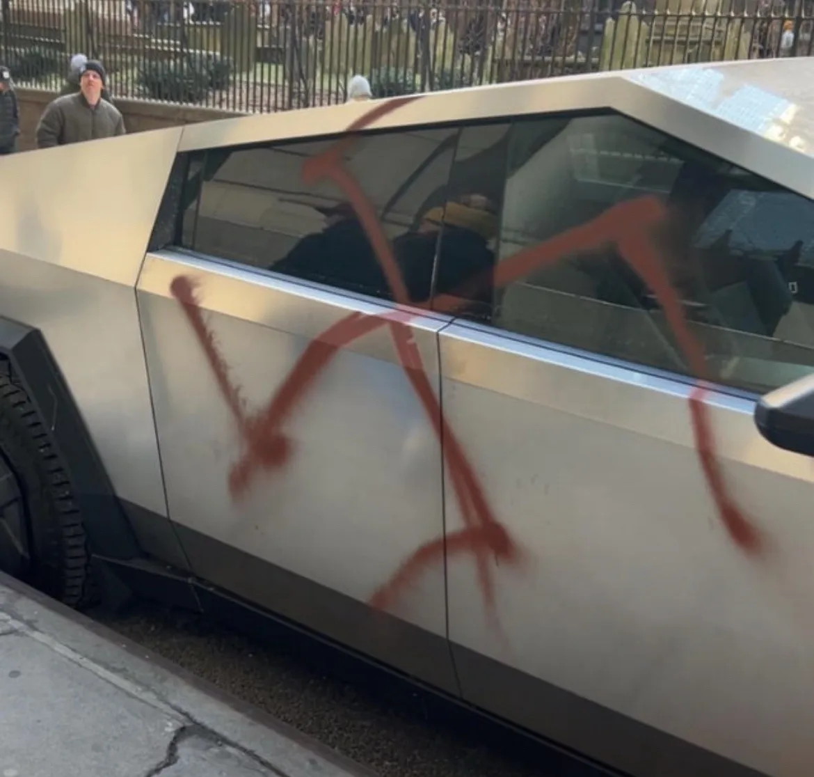 a silver, angular, futuristic-looking car, resembling a Tesla Cybertruck, is parked on a city street with large red…