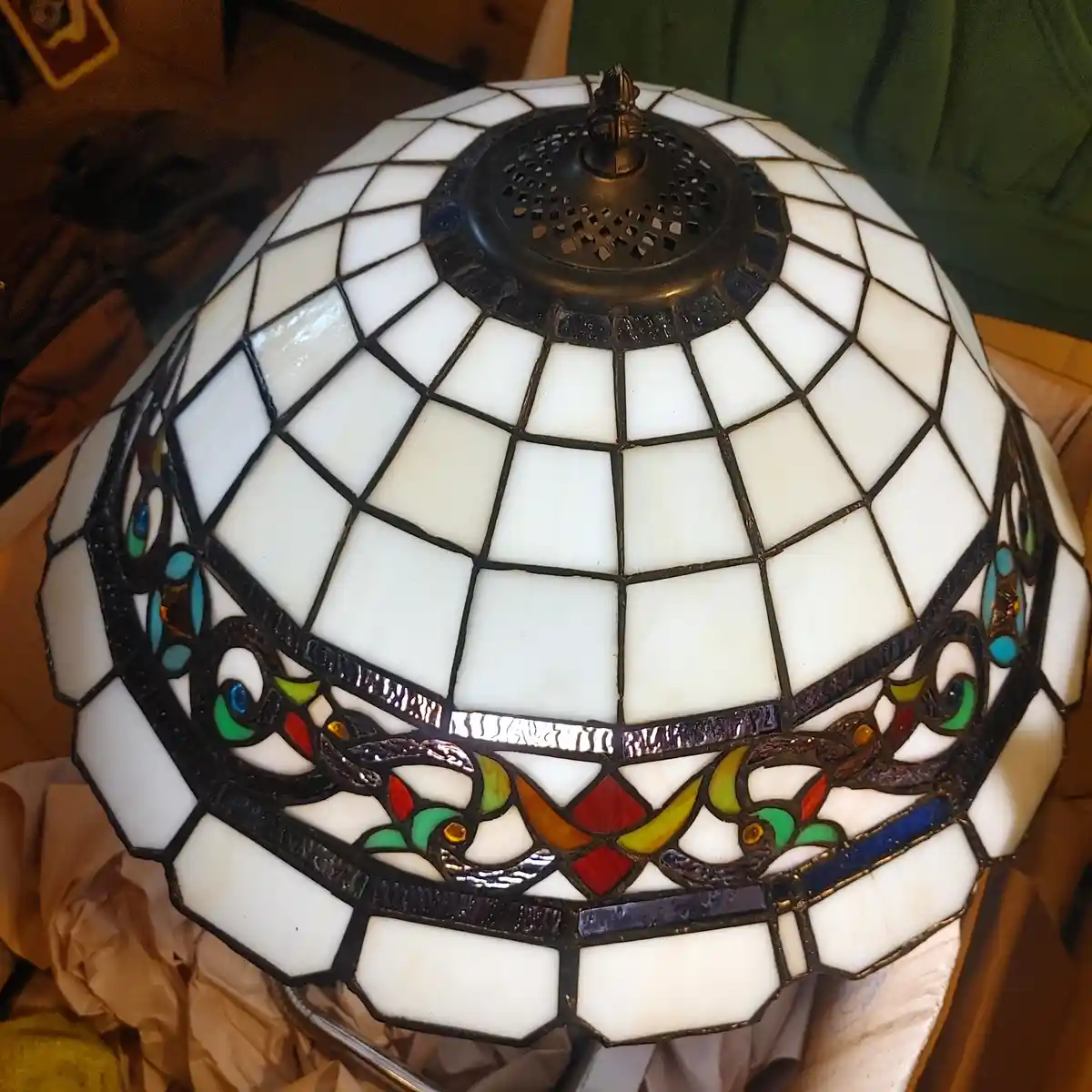 A close-up photo of a stained-glass lampshade with a geometric white pattern and colorful floral motifs around the middle…