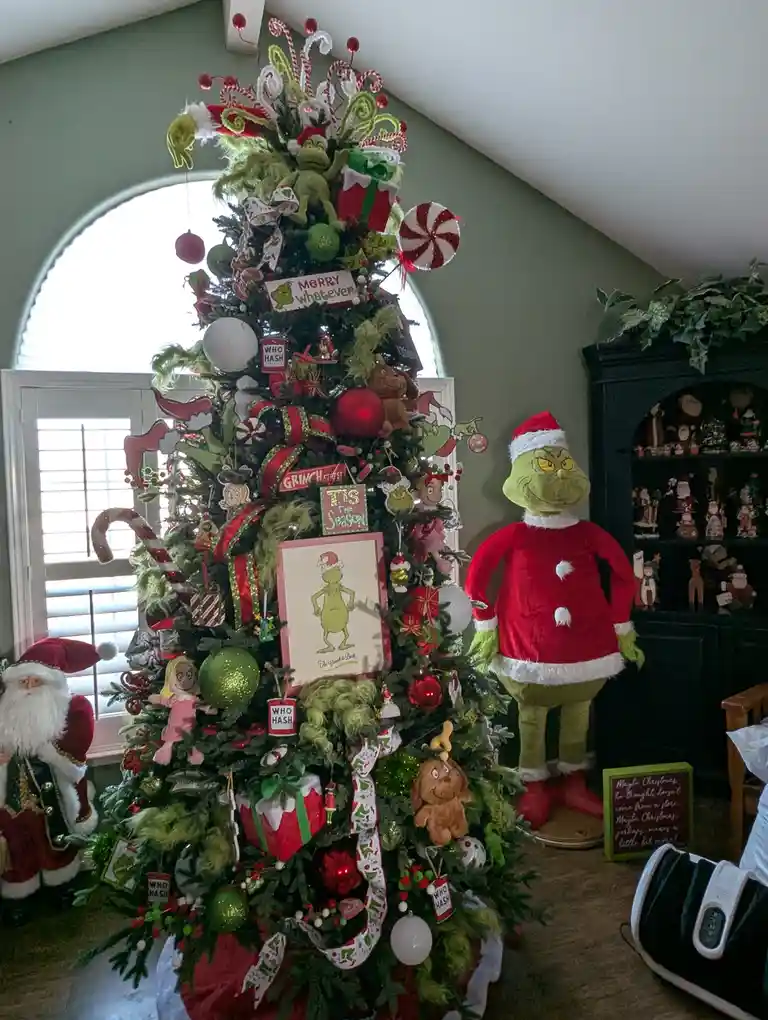 A heavily decorated Christmas tree is adorned with Grinch-themed ornaments, including candy canes, 'Who Hash' signs, and a…