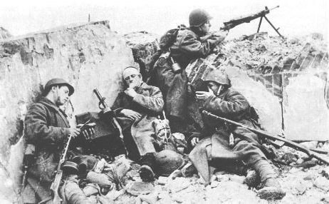A black-and-white historical photo shows four soldiers in a trench during wartime, appearing exhausted and weary. One…