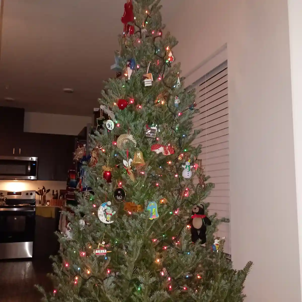 A decorated christmas tree with multicolored lights and various ornaments, including a snowman, a bear, and a 'cola' sign…