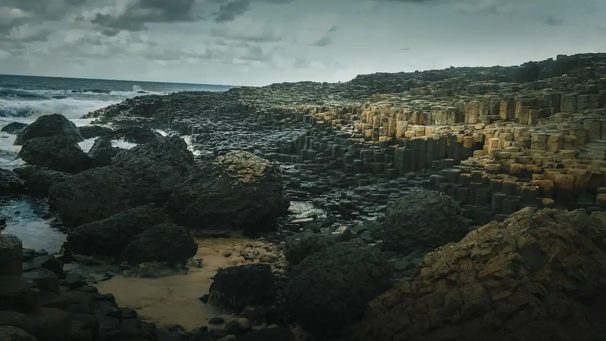 A dramatic landscape photo of the Giant's Causeway in Northern Ireland, featuring thousands of hexagonal basalt columns…