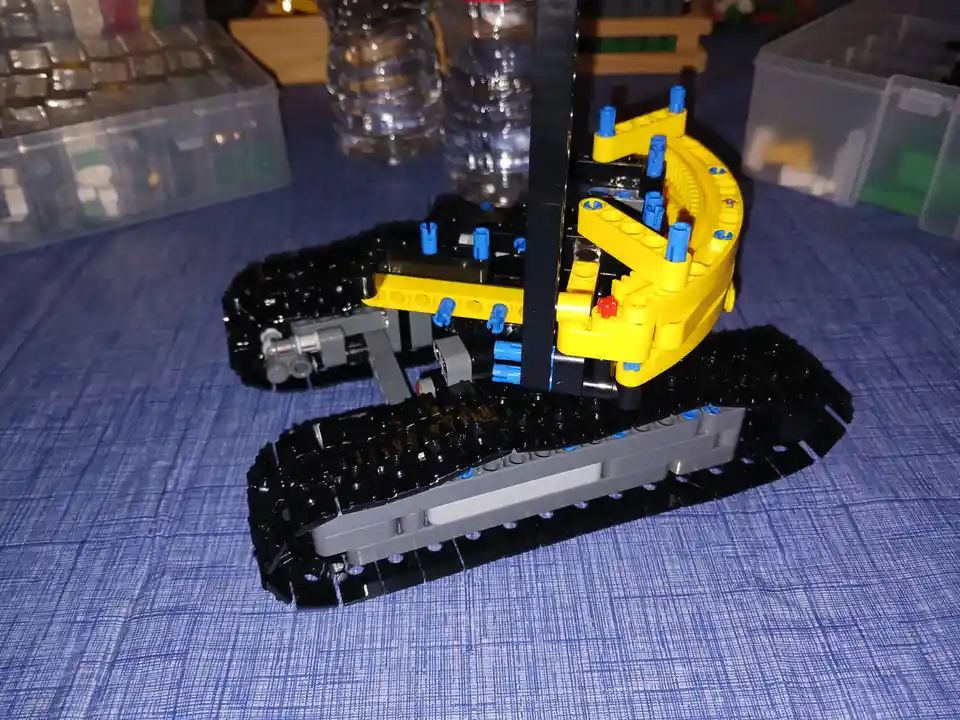 A close-up photo of a complex, custom-built LEGO Technic vehicle with black tracks, yellow and blue structural pieces, and…