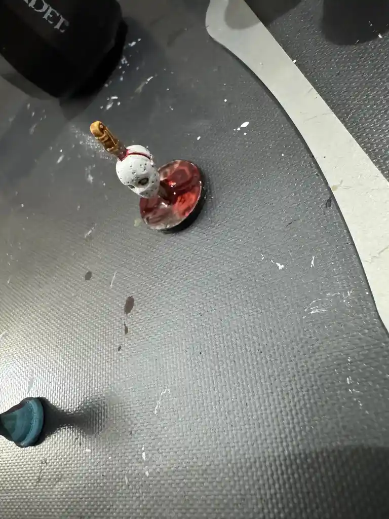 A small painted Jason Voorhees action figure with a white hockey mask and machete stands on a red-painted base, surrounded…