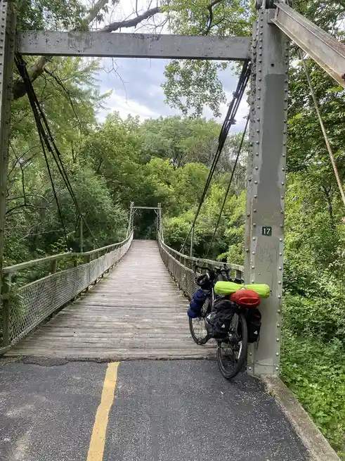 A bicycle heavily loaded with colorful panniers and gear is parked against the metal support pillar of a rustic wooden…