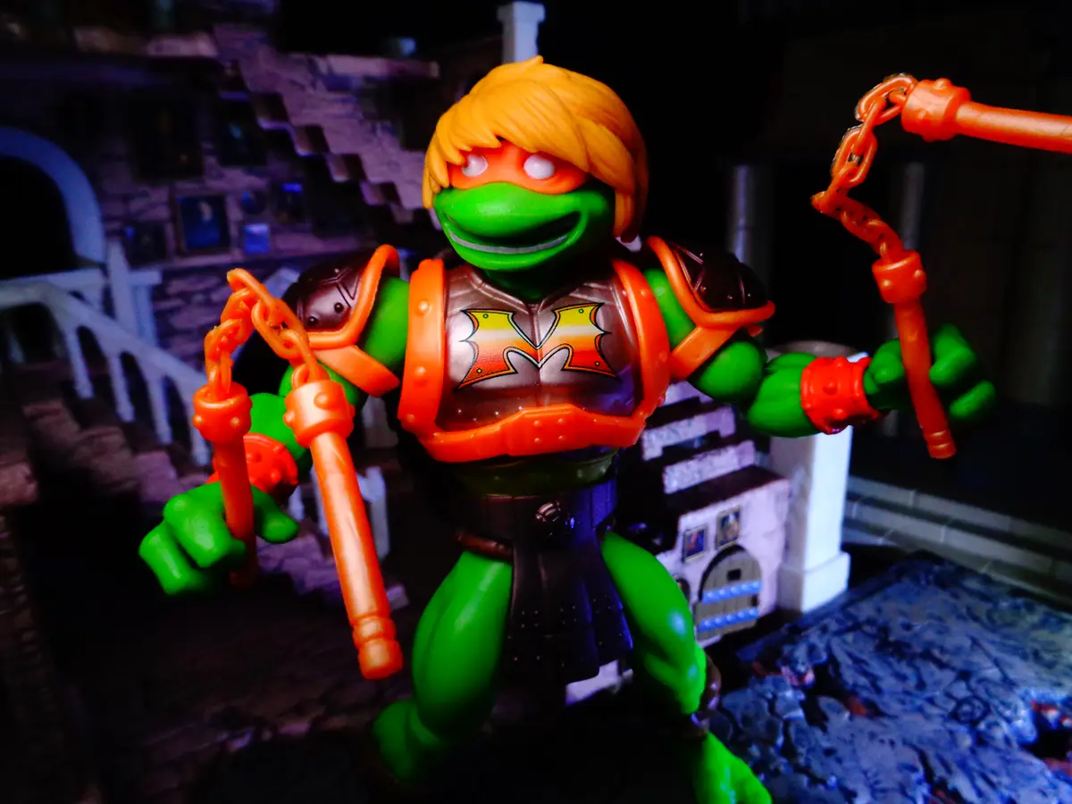 A green ninja turtle action figure with orange hair and an orange mask, wearing a brown and orange armored vest with a…