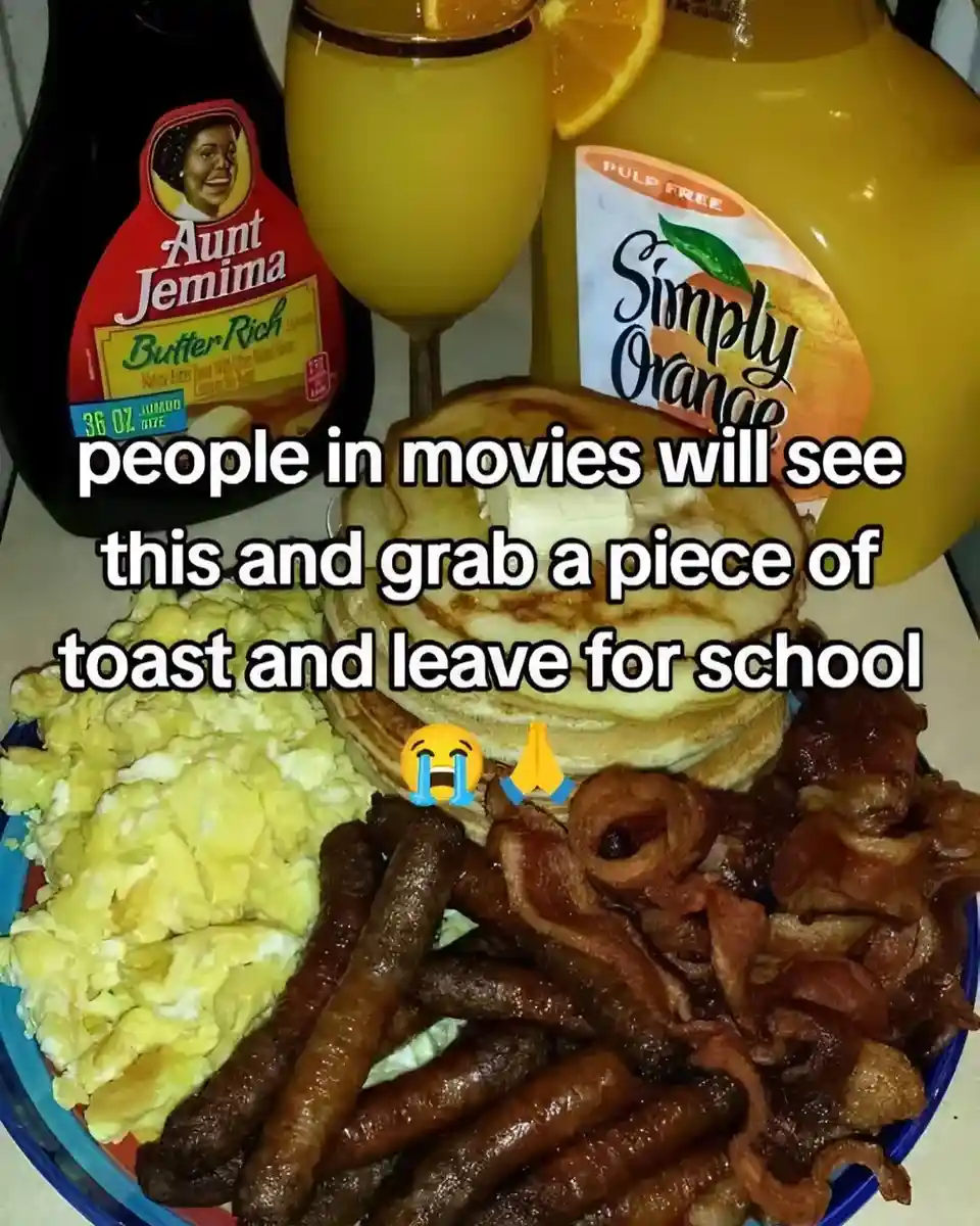 A lavish breakfast spread featuring scrambled eggs, bacon, sausage links, a stack of pancakes with butter, a glass of orange…