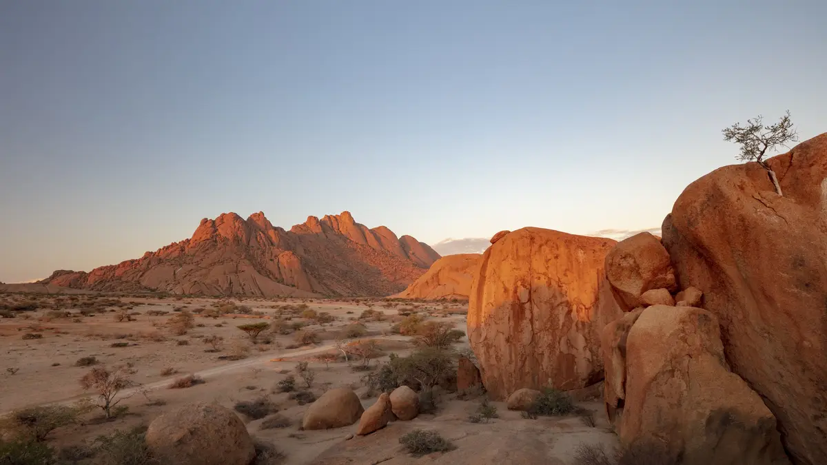 In Namibia's vast Namib Desert, the sun sets over the Spitzkoppe Nature Reserve, where jagged granite mountains meet the…