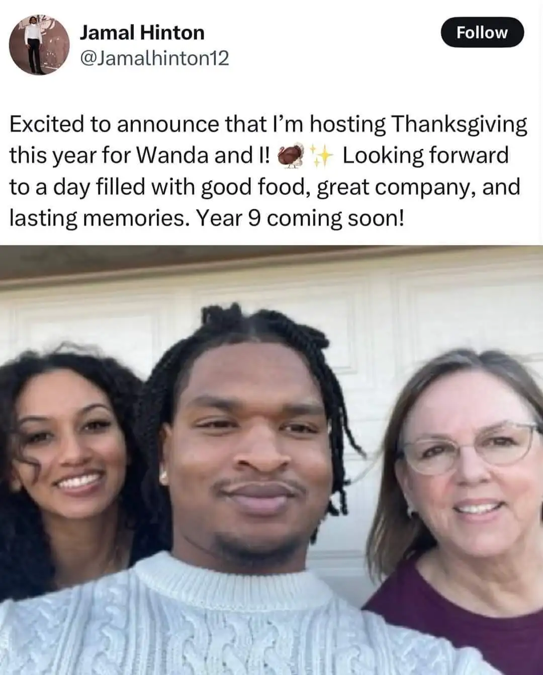 A selfie shows three people smiling in front of a white garage door. The person in the center, a man with braided hair…