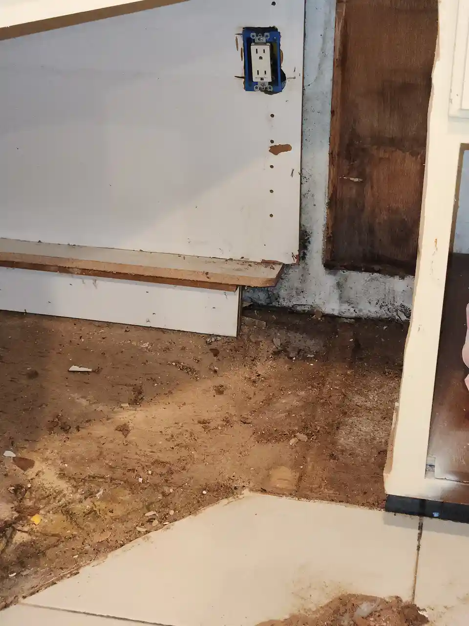 A close-up photo shows a partially demolished room with exposed drywall, dirt-covered floor, and a newly installed…