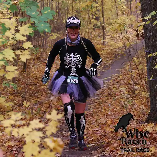 A woman in a full skeleton costume, including skull cap, face paint, skeleton shirt, tutu, and skeleton leggings, is running…
