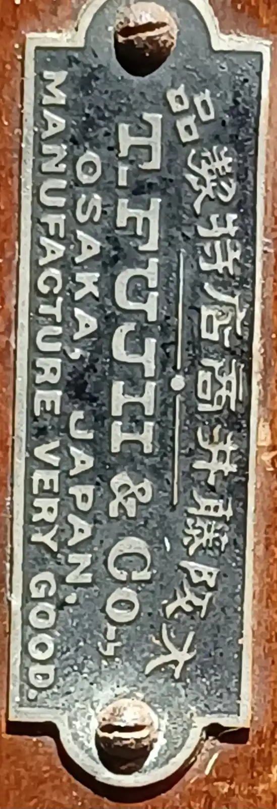 A close-up of a vintage metal plaque with raised lettering, showing Japanese kanji on the right and English text on the…