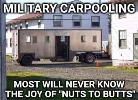 A large, beige, military-style trailer with multiple small windows and an open door is parked on a gravel lot in front of a…